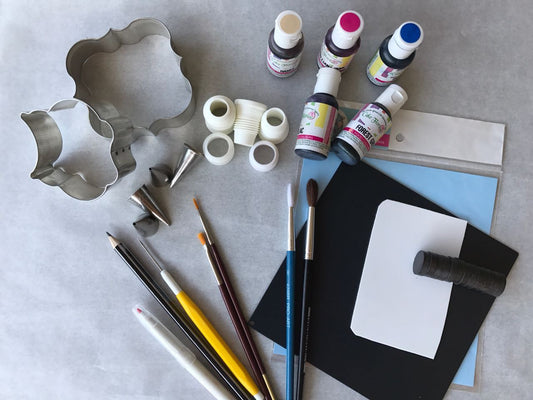 Assorted biscuit decorating tools, cookie cutters, food coloring bottles, and brushes on a table.