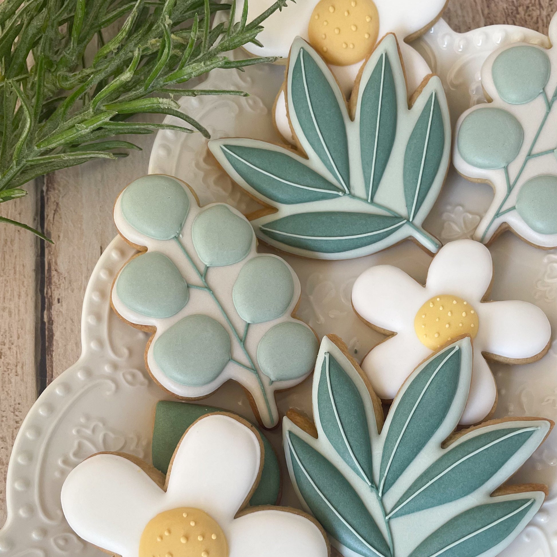 A cookies in the shape of an eucalyptus branch with green leaves by Biscuit Studio.